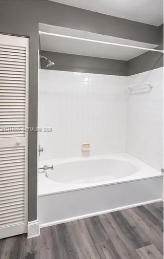 Oval soaking tub with a white tile surround, brushed metal fixtures, integrated soap dish, and wood-finish flooring