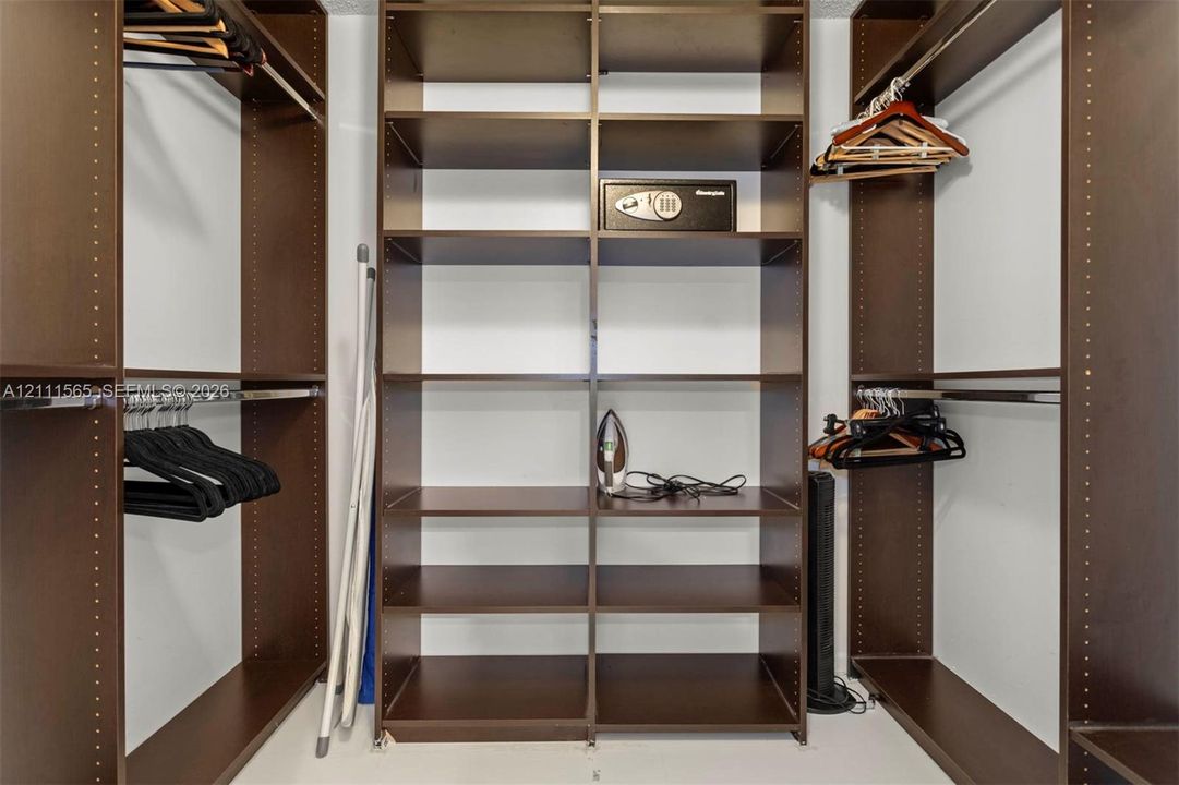 Walk-in closet featuring floor-to-ceiling built-in dark wood-finish shelving and metal garment hanging rods