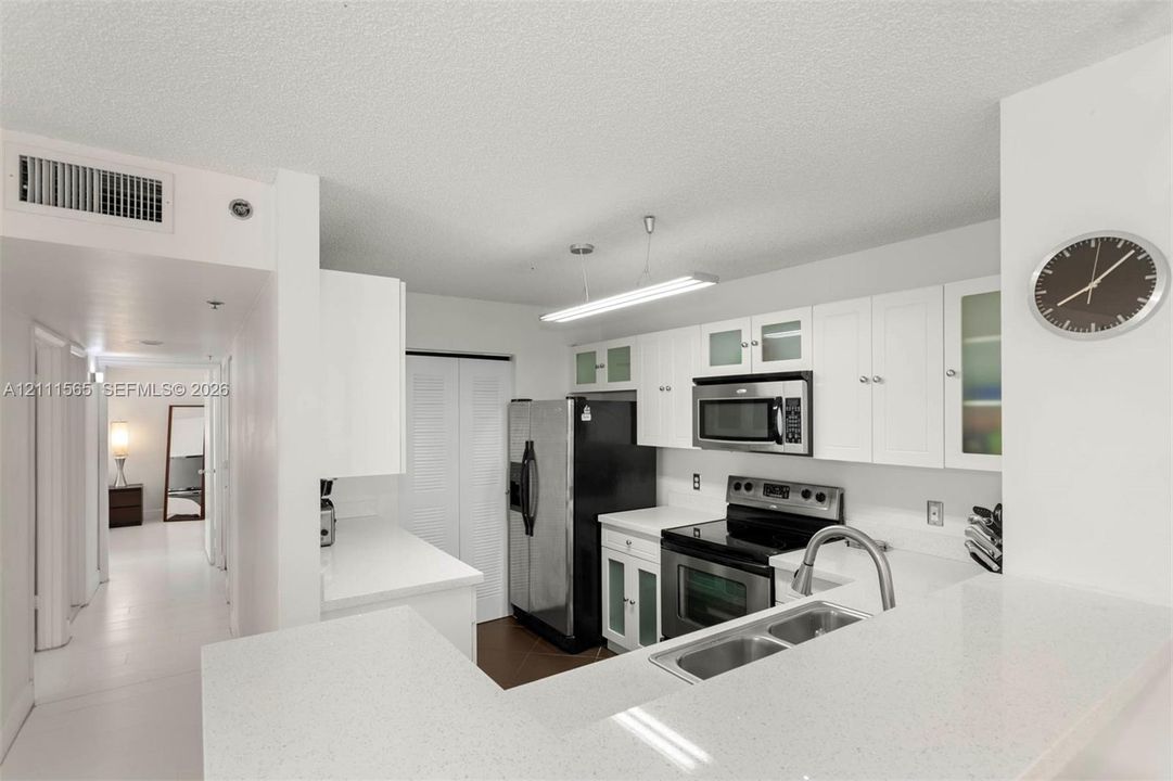 Kitchen featuring white shaker-style cabinetry with glass-front accents, solid-surface countertops, stainless steel appliances, and a dual-basin sink with a gooseneck faucet