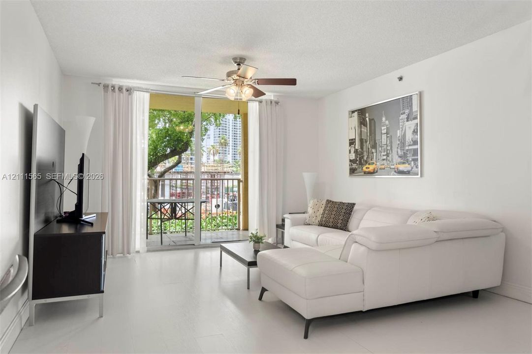 Living space featuring white flooring, a ceiling fan with integrated lighting, and glass sliding doors opening to a balcony