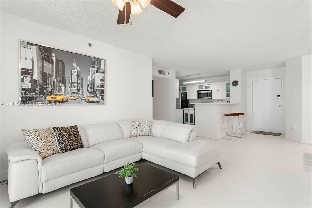 Open-concept living space featuring solid-surface flooring, a ceiling fan with light fixture, and kitchen cabinetry with a breakfast bar