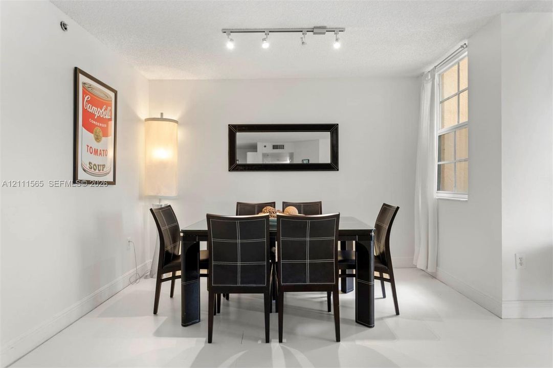 Neutral-toned interior space featuring overhead track lighting, a wall-mounted rectangular mirror with a black frame, and a multi-pane window