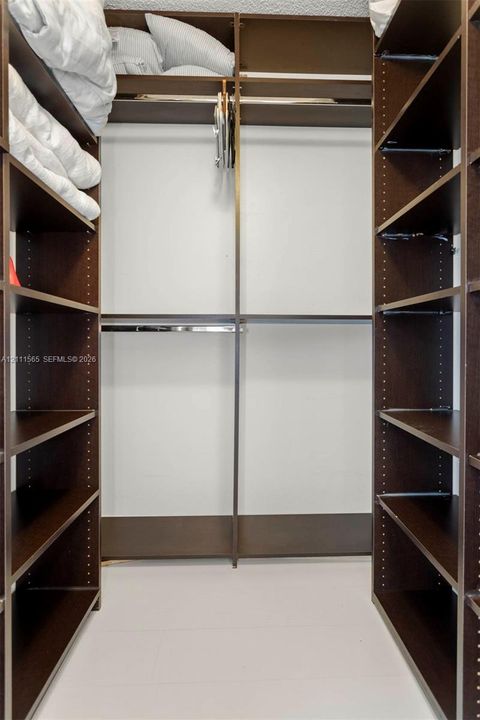 Walk-in closet featuring dark wood-finish cabinetry, adjustable shelving, and dual metal hanging rods