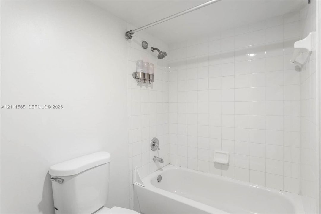 Full-size bathtub featuring white square-tile surround, chrome wall-mounted fixtures, and integrated soap dish