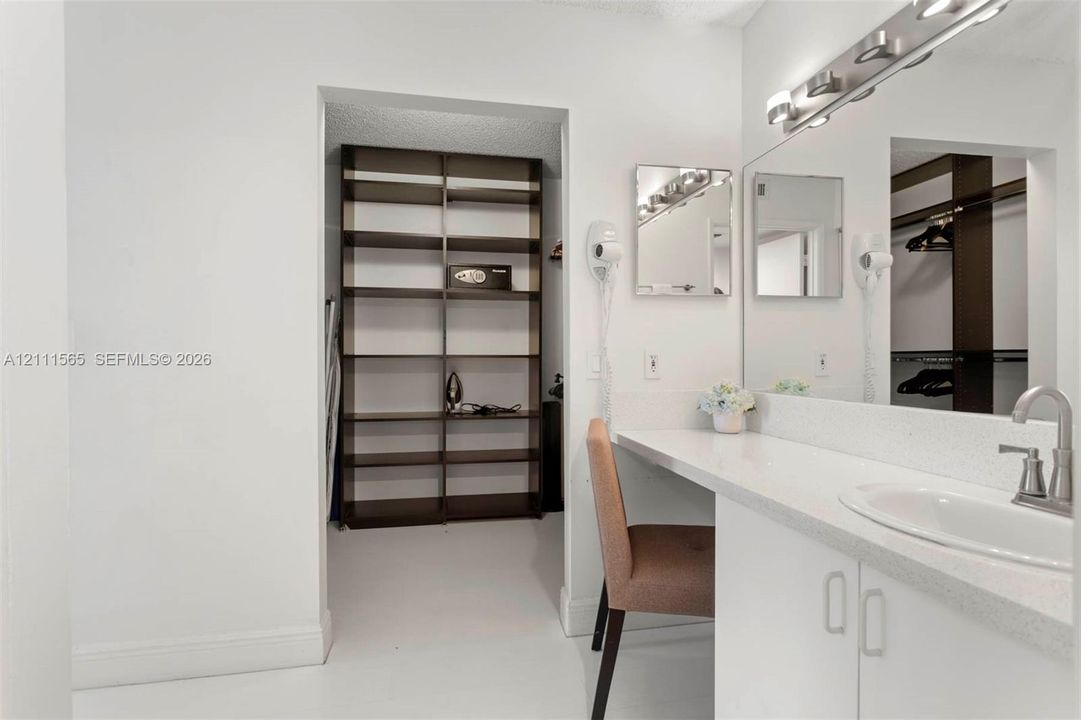 Bathroom vanity featuring a quartz countertop, integrated sink, large wall-to-wall mirror, built-in lower cabinetry, and an open-concept walk-in storage area with fixed shelving