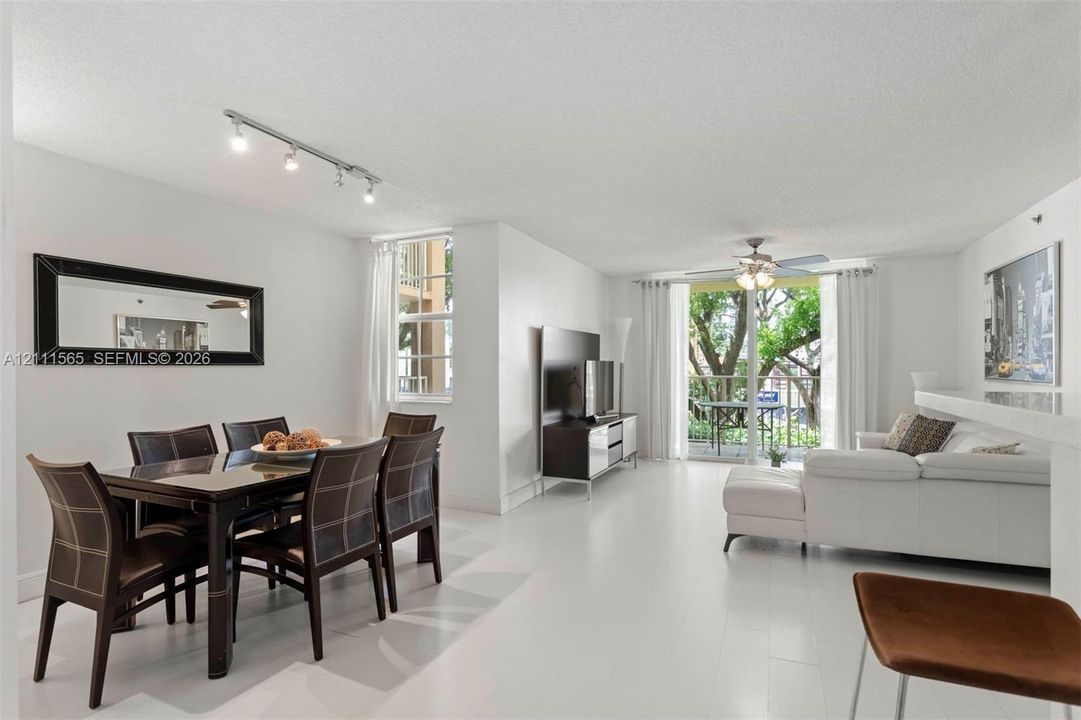 Open-concept living space featuring wood-finish flooring, recessed track lighting, a ceiling fan with integrated light fixture, and floor-to-ceiling glass sliding doors providing exterior access