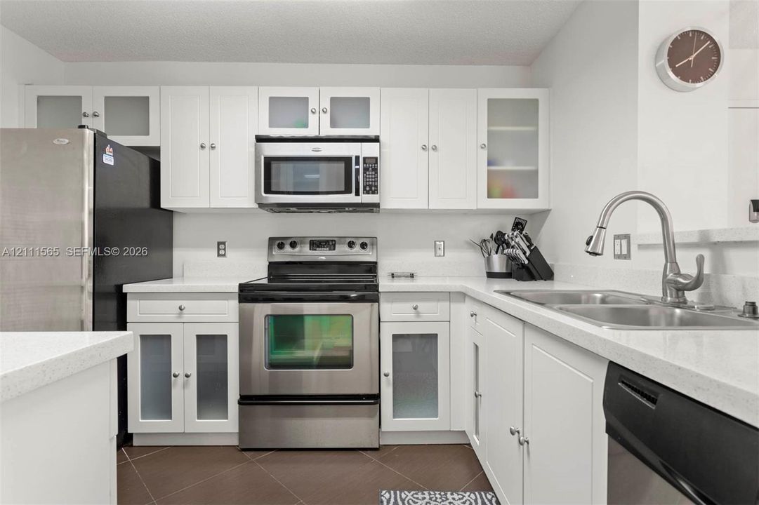 Kitchen featuring white shaker-style cabinetry with frosted glass inserts, stainless steel appliances, solid surface countertops, and an undermount dual-basin sink with a pull-down faucet