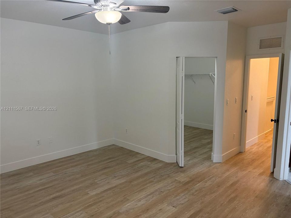 Wood-finish flooring, vaulted ceiling, and ceiling fan with integrated lighting, featuring a walk-in closet with wire shelving