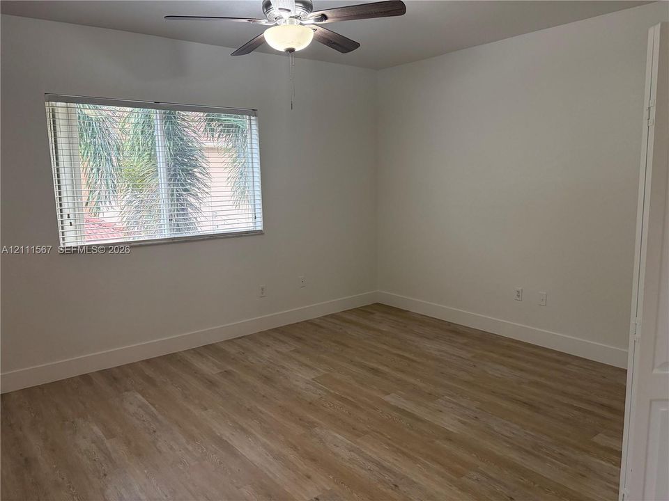 Wood-finish flooring, neutral wall tones, multi-pane window with horizontal blinds, and a ceiling-mounted light fixture with fan