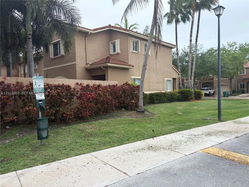 Two-story stucco exterior featuring a tile roof, mature palm trees, landscaped shrubbery, and a concrete sidewalk