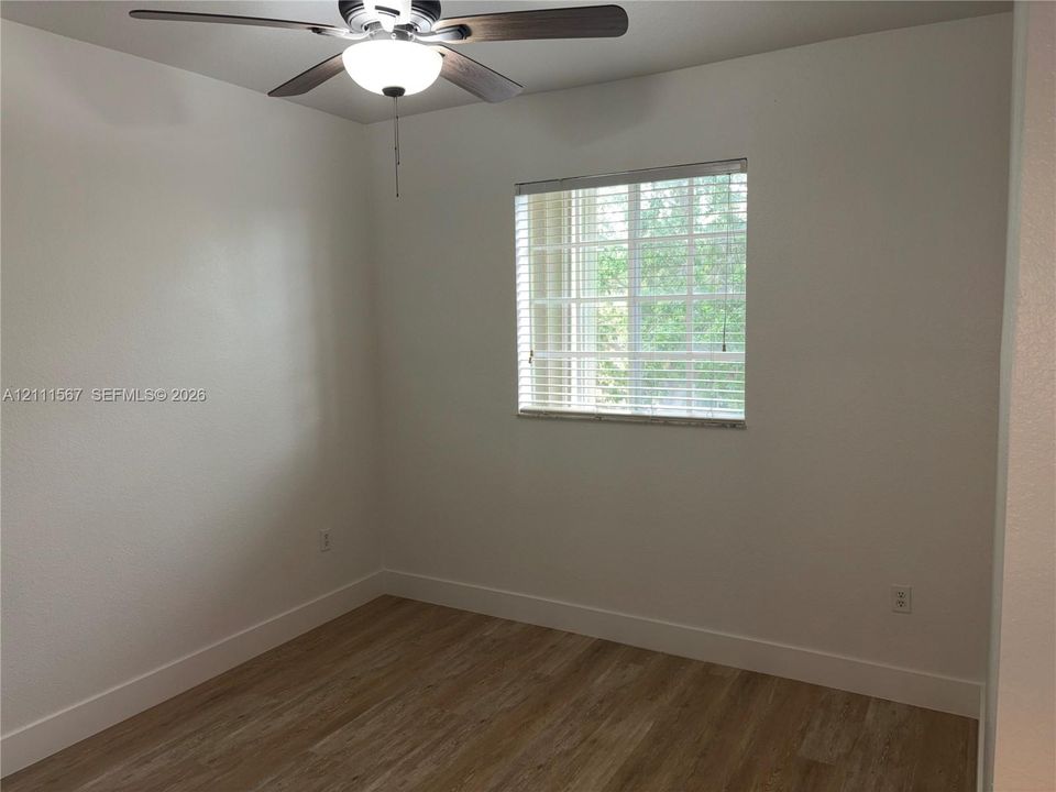 Interior room featuring wood-finish flooring, a multi-blade ceiling fan with integrated light fixture, and a single-pane window with horizontal blinds
