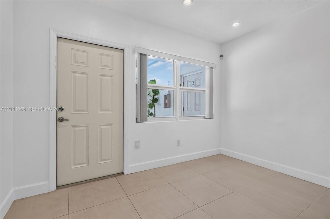 Neutral-toned tile flooring, recessed ceiling lighting, and a multi-panel entry door featuring a brushed metal deadbolt and lever handle