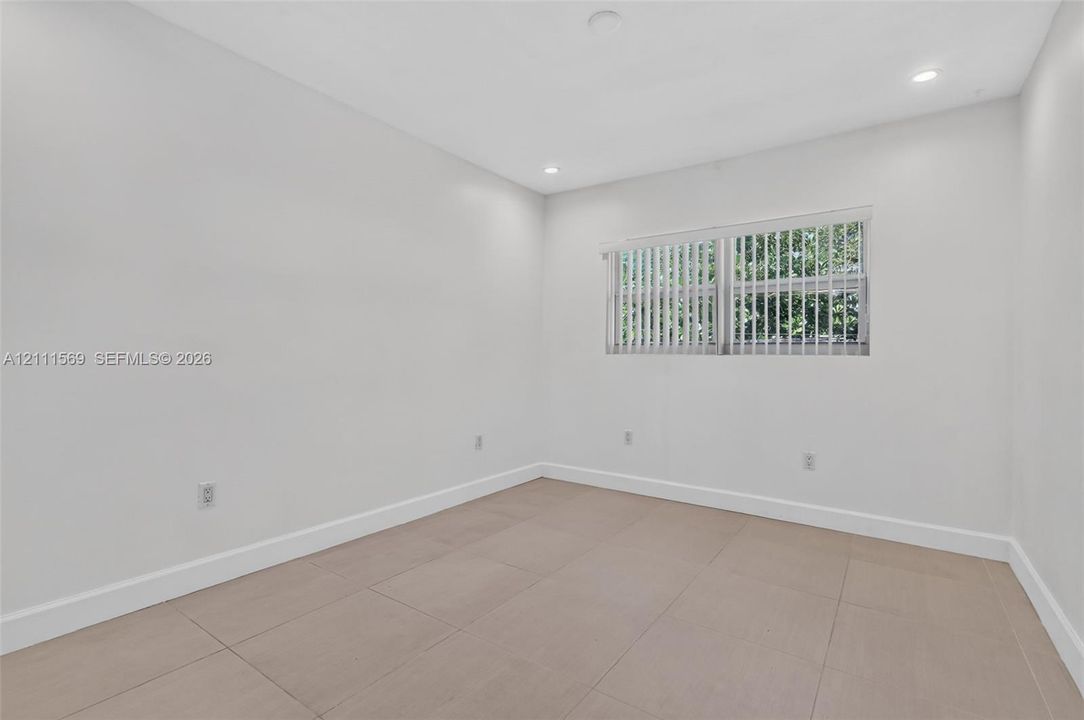 Neutral-toned tile flooring, recessed ceiling lighting, and large-format horizontal window with vertical blinds