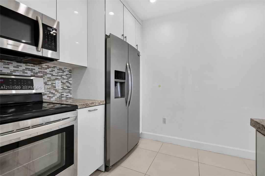 Kitchen featuring white gloss cabinetry, stone-finish countertops, stainless steel appliances, and a glass-tile backsplash