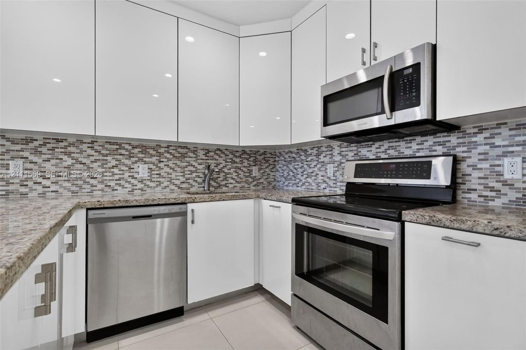 Kitchen featuring high-gloss white cabinetry, stone-finish countertops, stainless steel appliances, and a glass-tile mosaic backsplash