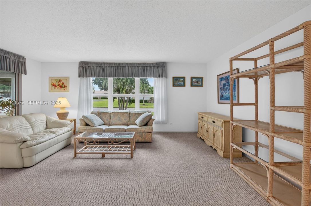 Living area featuring neutral berber carpeting, triple-panel impact window, and recessed sliding glass door leading to enclosed FL room