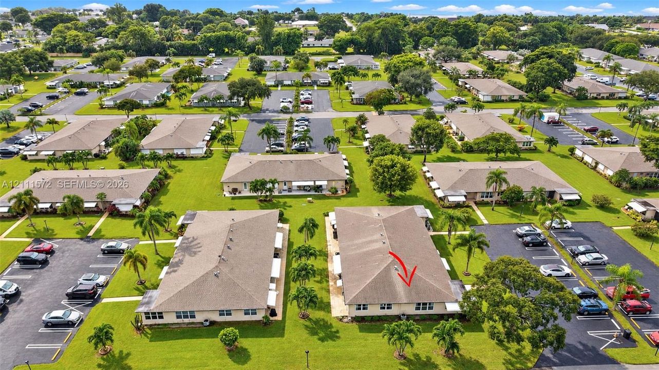Aerial perspective of a multi-unit residential property featuring low-pitched shingle roofing, paved surface parking, and mature palm landscaping
