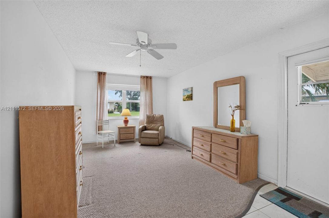 Primary bedroom with berber carpeting, a central ceiling fan, and large impact windows providing natural light, energy efficiency, and sound proofing