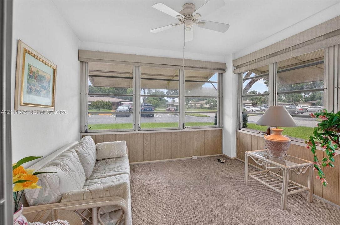 Enclosed sunroom featuring expansive paneled windows, berber carpeting, and a ceiling fan