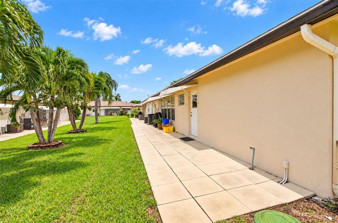 Back patio featuring an expansive paved walkway, mature palm trees, and a level grass lawn where you can create your garden