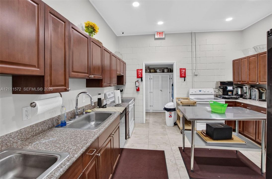 Kitchen featuring dark wood cabinetry, stone-finish countertops, dual stainless steel sinks, recessed lighting, and tile flooring