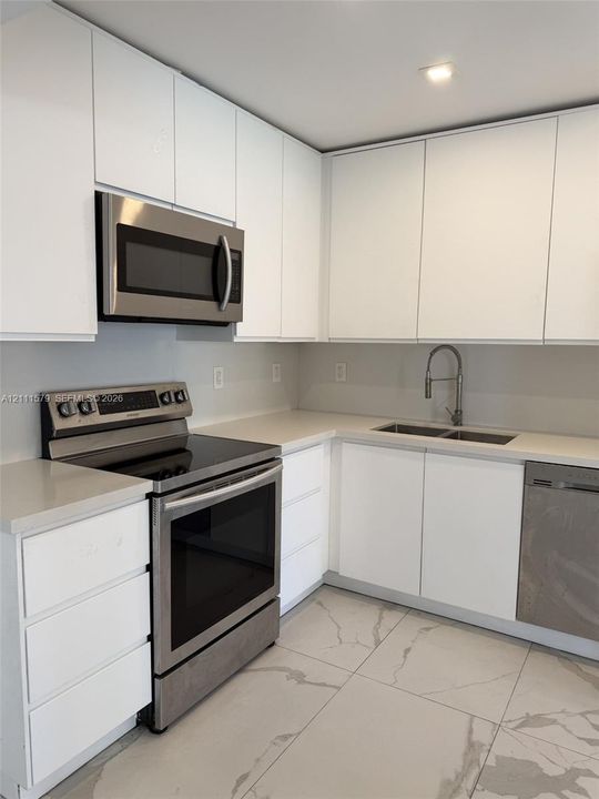 Kitchen featuring flat-panel white cabinetry, solid-surface countertops, stainless steel appliances, a dual-basin sink with a gooseneck faucet, and large-format porcelain tile flooring