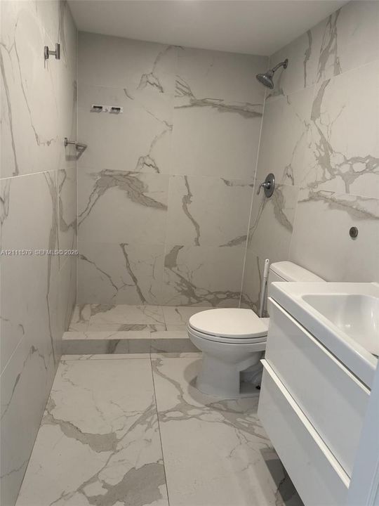 Walk-in shower enclosure featuring large-format stone-patterned tile, white floating vanity, and chrome fixtures