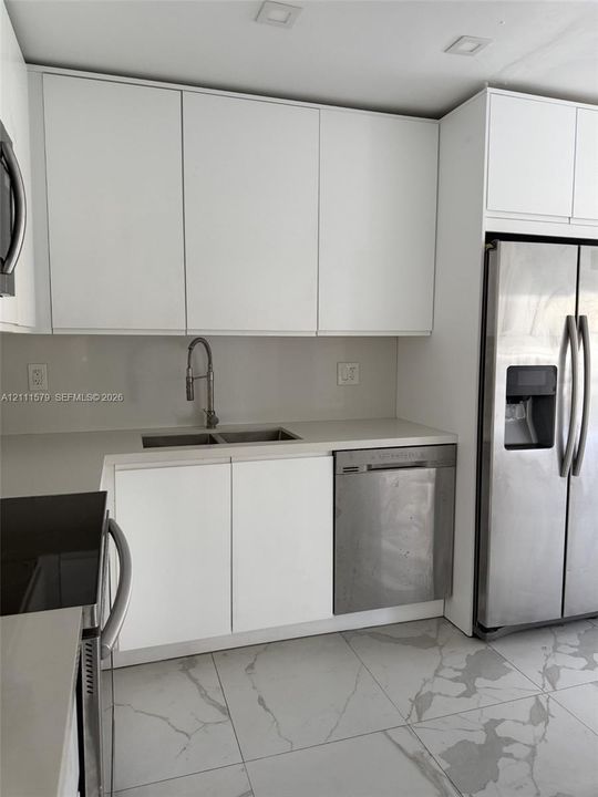 Modern kitchen featuring flat-panel white cabinetry, solid-surface countertops, recessed ceiling lighting, stainless steel appliances, and large-format tile flooring