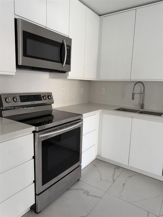 Contemporary kitchen featuring white flat-panel cabinetry, light-toned stone-style countertops, stainless steel appliances, a dual-basin undermount sink with a gooseneck faucet, and large-format tile flooring