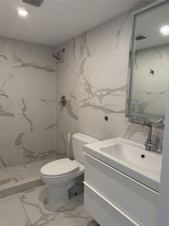 Full-height wall tiling with a vein-pattern finish, modern white floating vanity, integrated rectangular sink, wall-mounted backlit mirror, and recessed overhead lighting