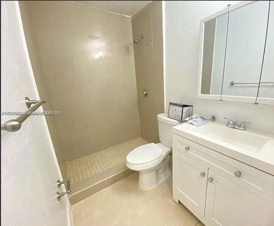 Walk-in shower with tiled surround, white vanity cabinet, integrated countertop sink, and mirrored medicine cabinet