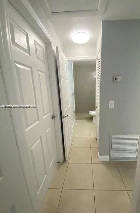 Hallway featuring neutral tile flooring, six-panel interior doors, and a louvered closet door