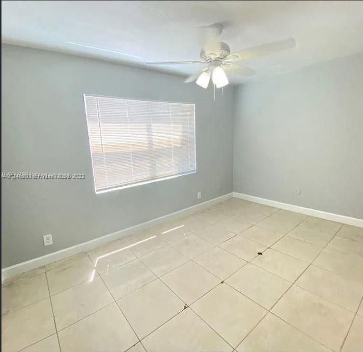 Neutral wall tones, large-format tile flooring, window with horizontal blinds, and a ceiling-mounted fan with integrated light fixture