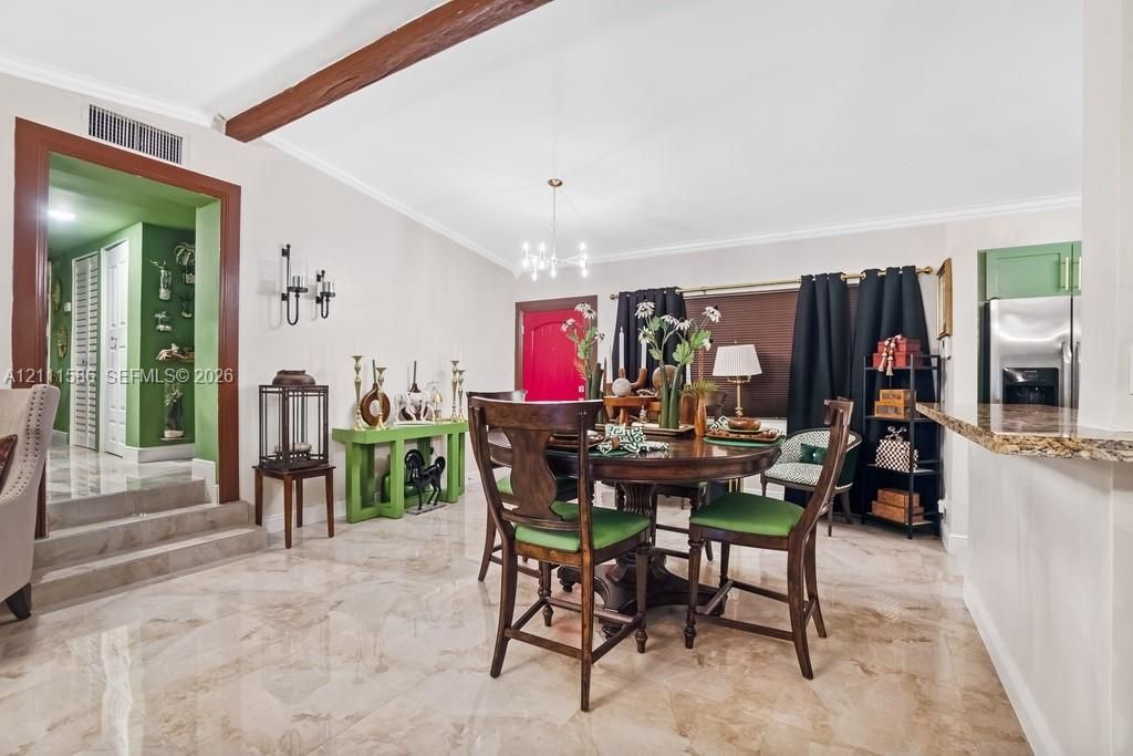 Polished stone tile flooring, exposed wood ceiling beam, multi-arm chandelier, and a breakfast bar with stone-surfaced countertop
