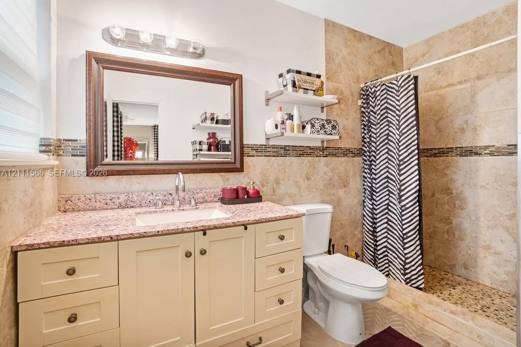 Bathroom featuring a vanity with a speckled countertop, integrated sink, and wood-toned cabinetry, paired with a shower enclosure showcasing natural stone wall tiles, a pebble-finish floor, and a decorative tile inlay
