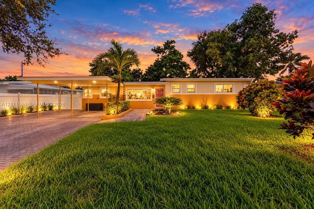 Single-story exterior featuring a paved brick driveway, attached carport, white privacy fencing, and professional landscaping