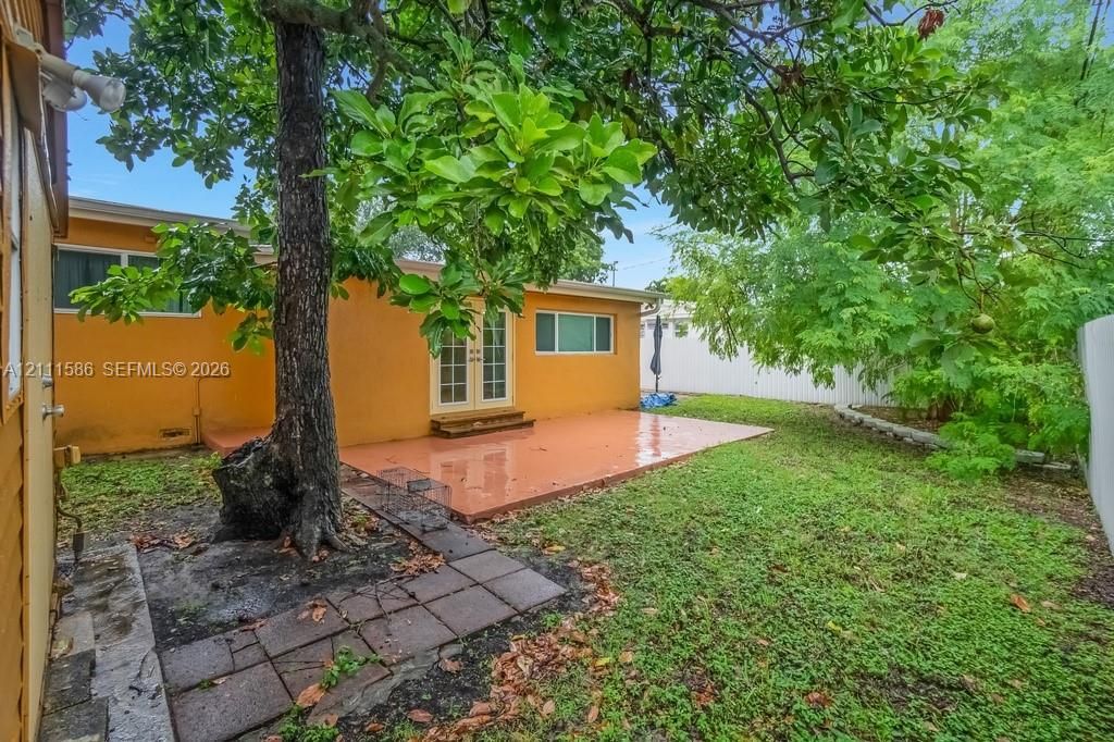 Rear exterior featuring a concrete patio, French doors, mature tree, stone-tile walkway, and privacy fencing