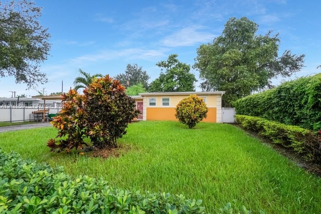 Exterior view featuring a fenced yard with manicured lawn, established shrubbery, and a private side gate