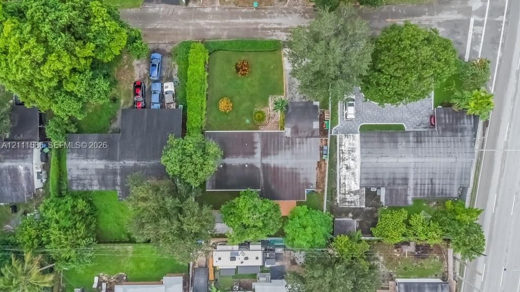Aerial perspective featuring a manicured lawn, paved driveway, mature trees, and shingled roof structures