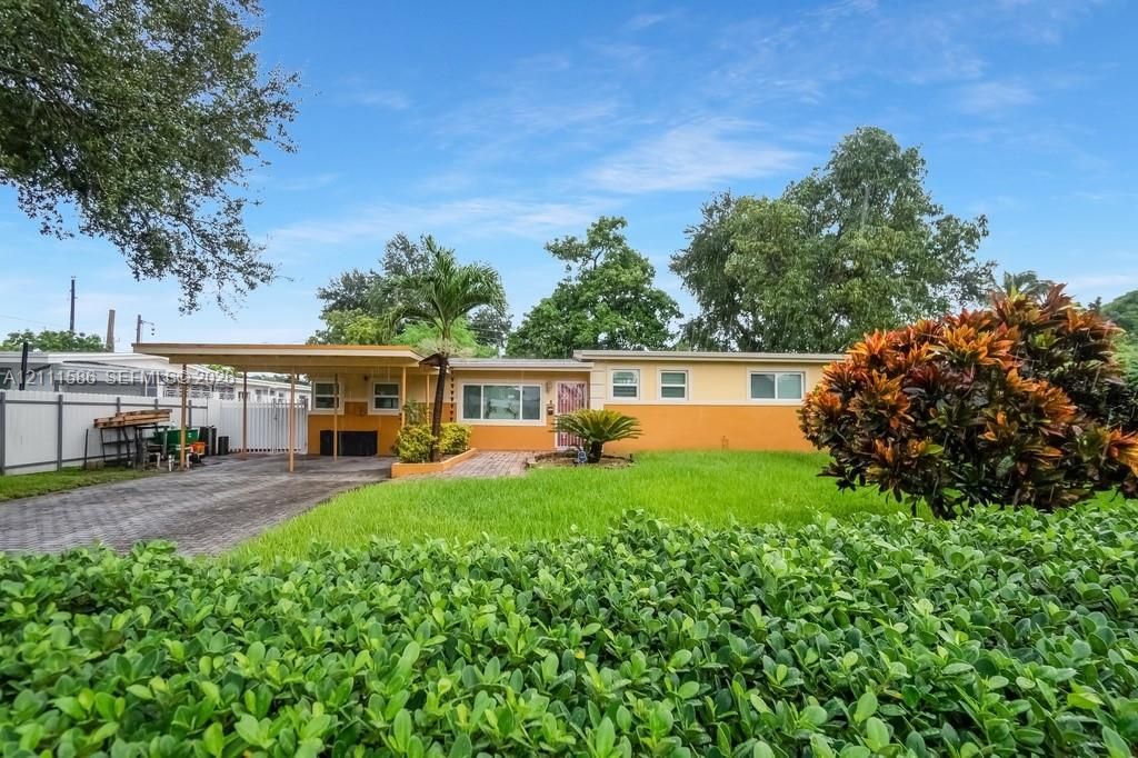 Single-story residence featuring a two-tone exterior, attached carport, paver driveway, manicured lawn, and privacy fencing
