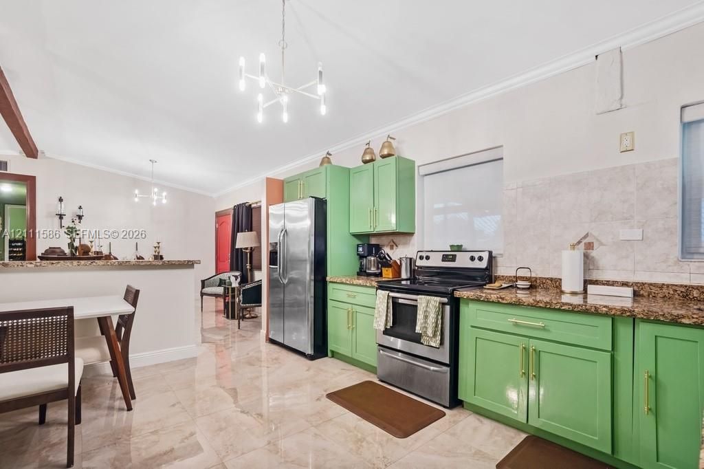 Kitchen featuring green cabinetry, stone-finish countertops, tile backsplash, polished stone-finish flooring, and modern multi-arm chandelier lighting