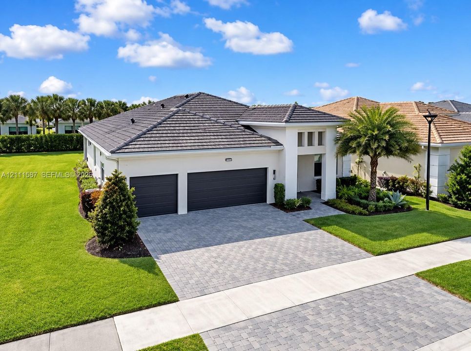Single-story residence featuring a concrete tile roof, a three-car garage, and a paver driveway