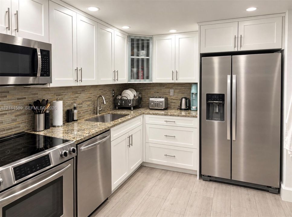 Kitchen featuring white shaker-style cabinetry, stainless steel appliances, stone-surface countertops, multi-toned tile backsplash, and wood-finish flooring