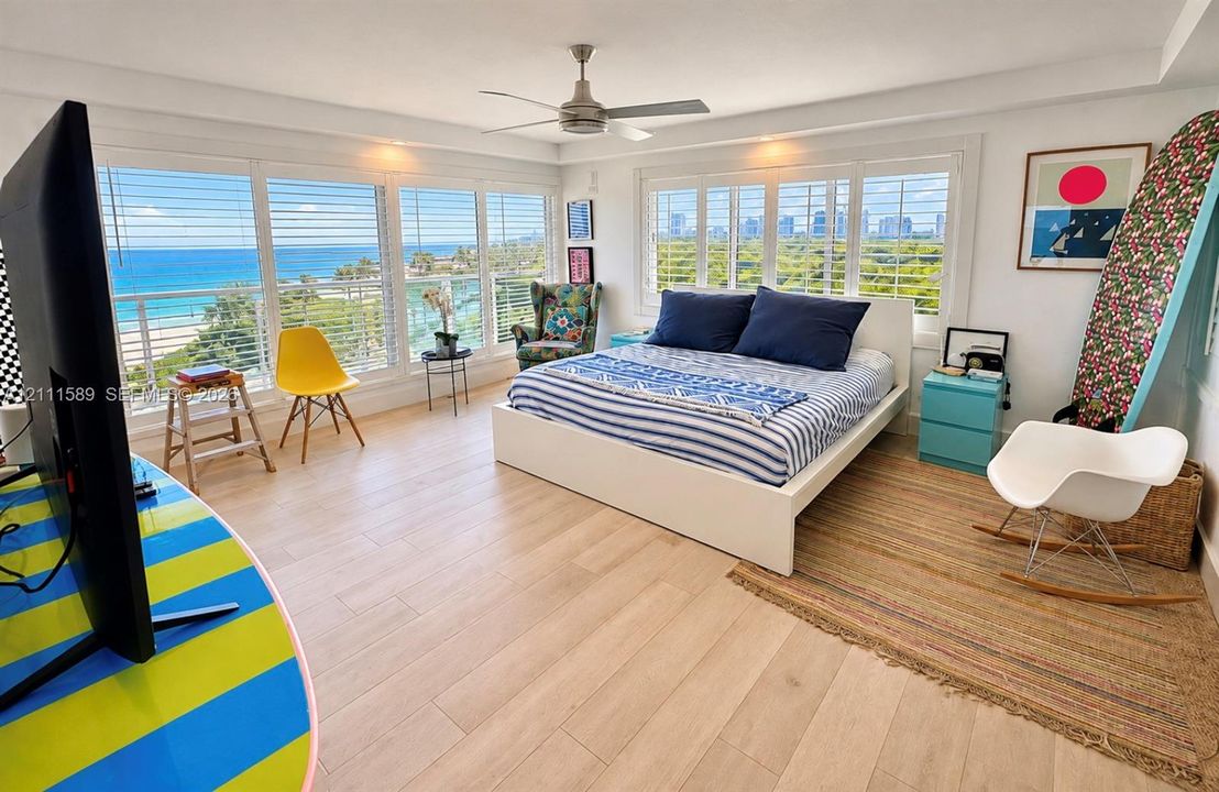 Extensive window walls with coastal scenery, wood-finish flooring, ceiling fan, and adjustable shutter window coverings