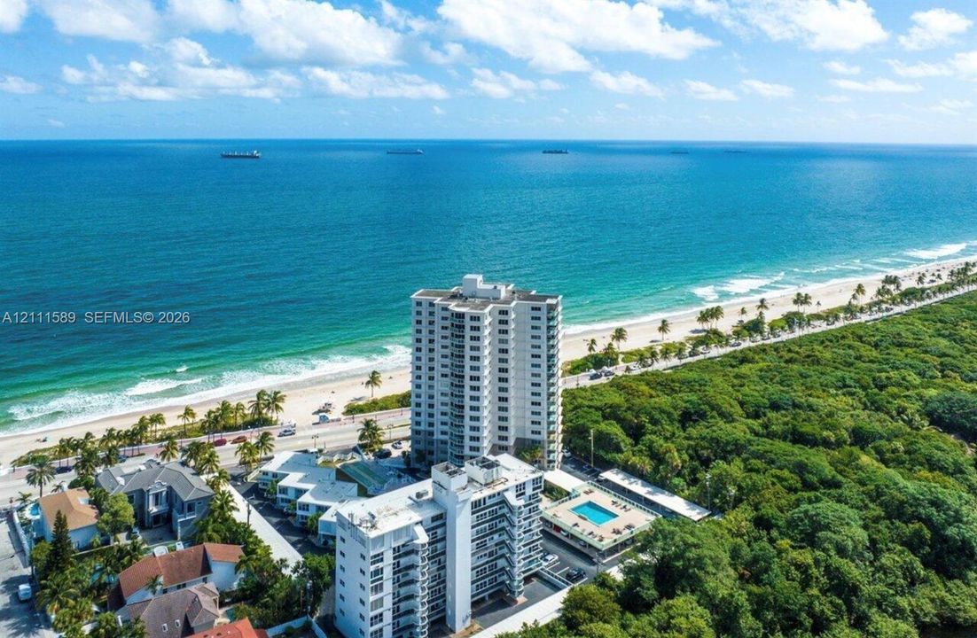 Aerial perspective of coastal high-rise buildings featuring a swimming pool, paved sundeck, and proximity to the shoreline