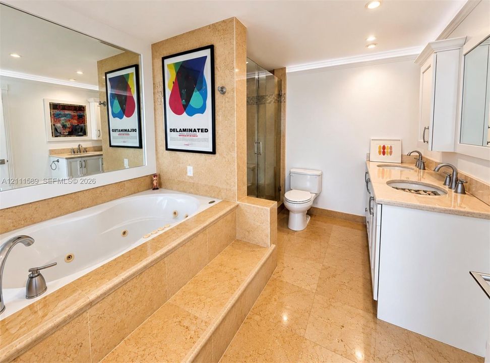 Jetted soaking tub with tile surround, walk-in glass shower, dual-sink vanity, and polished stone flooring
