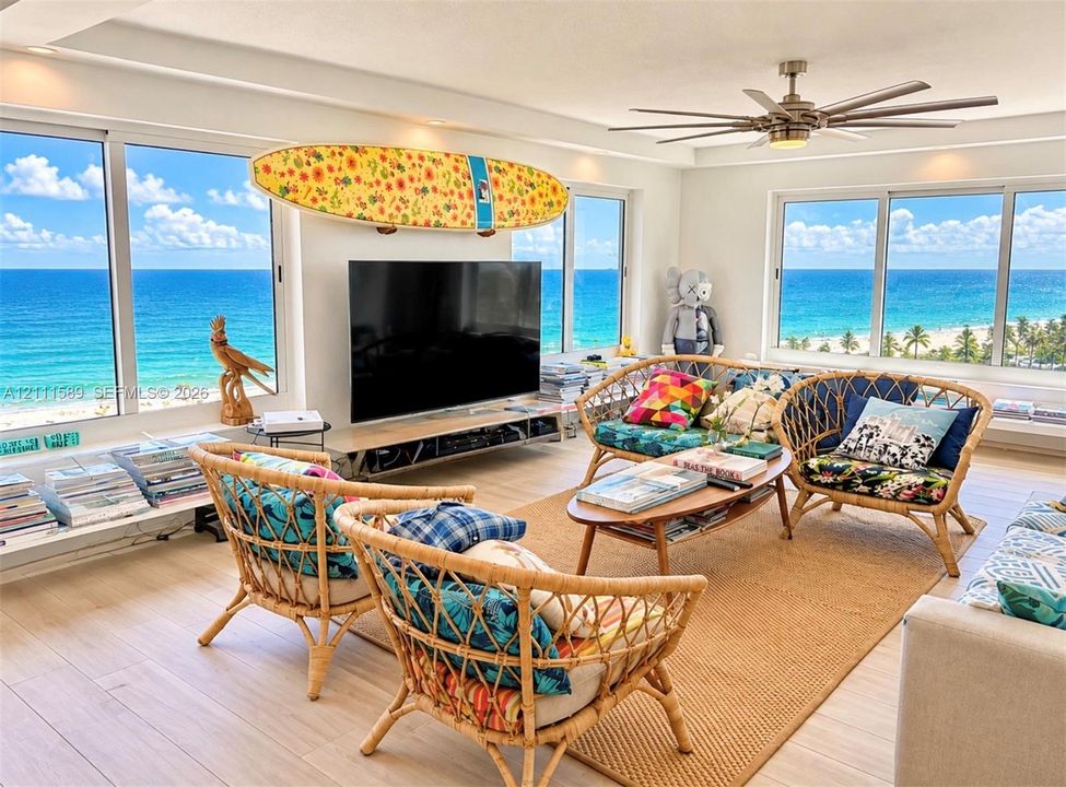 Expansive windows with ocean horizon exposure, light-toned wood-finish flooring, recessed lighting, and a multi-blade ceiling fan