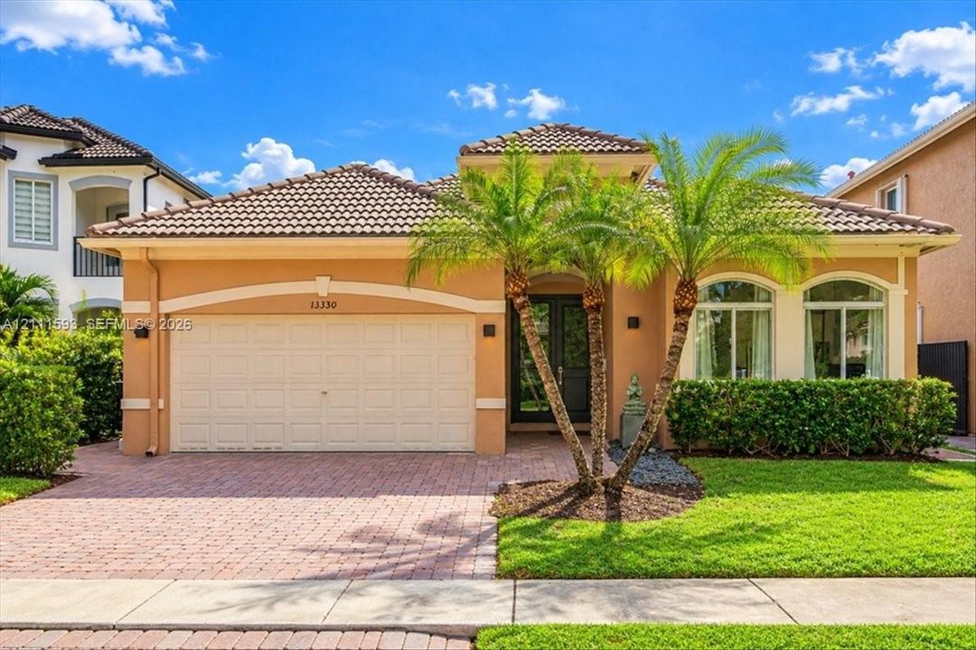 Single-story stucco exterior featuring a tiled hip roof, arched window detailing, an attached two-car garage, and paved driveway