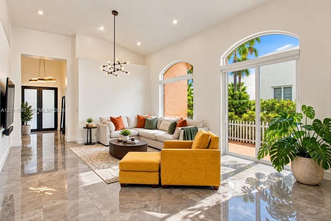 Vaulted ceilings featuring recessed lighting, polished stone-finish flooring, a modern sputnik-style chandelier, and large arched windows with sliding glass door access