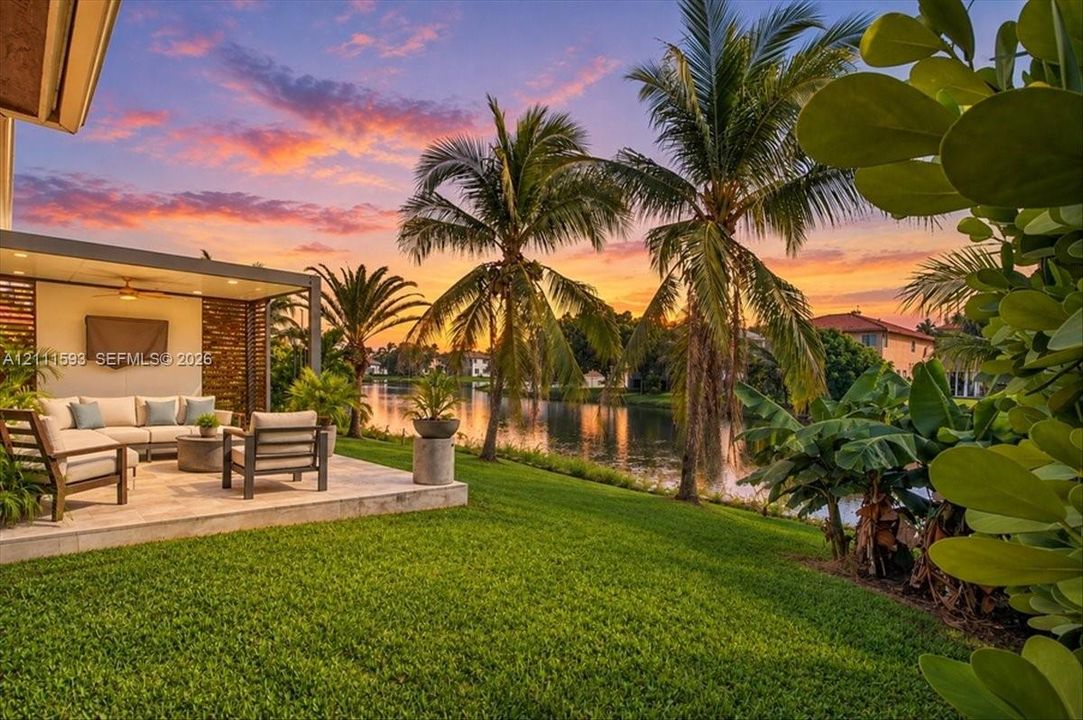 Lake-front property featuring a covered patio with recessed lighting, stone-tiled flooring, wood-slat screening, and established tropical landscaping